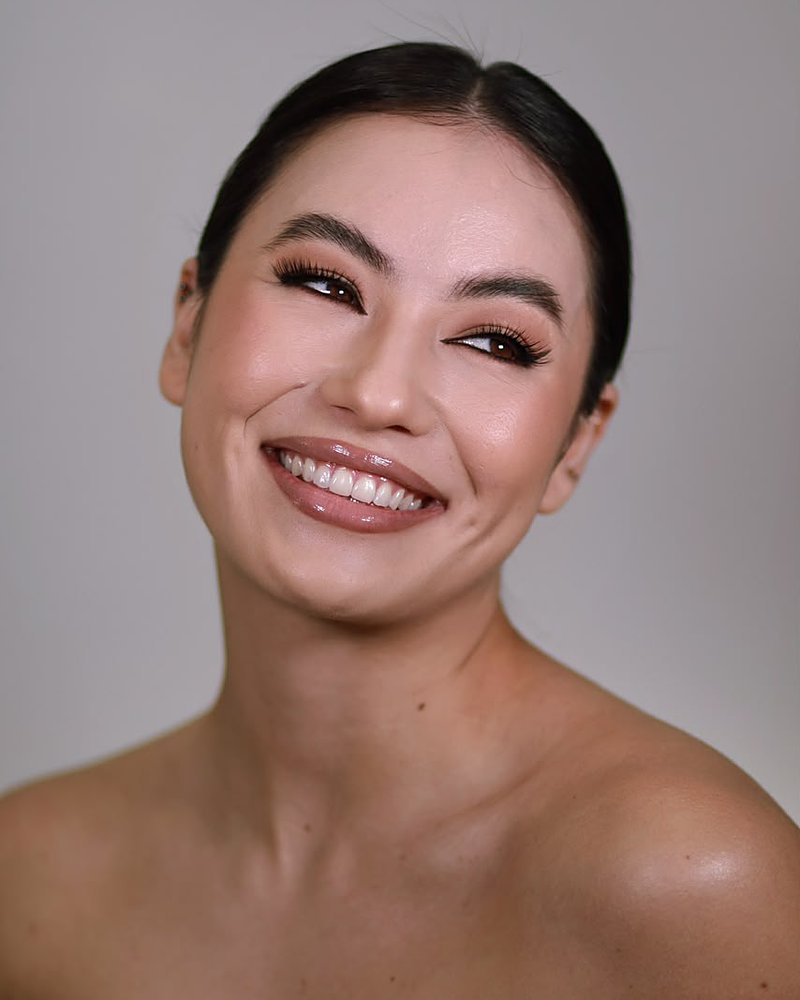 Modelo sorrindo, com cílios marcados e gloss